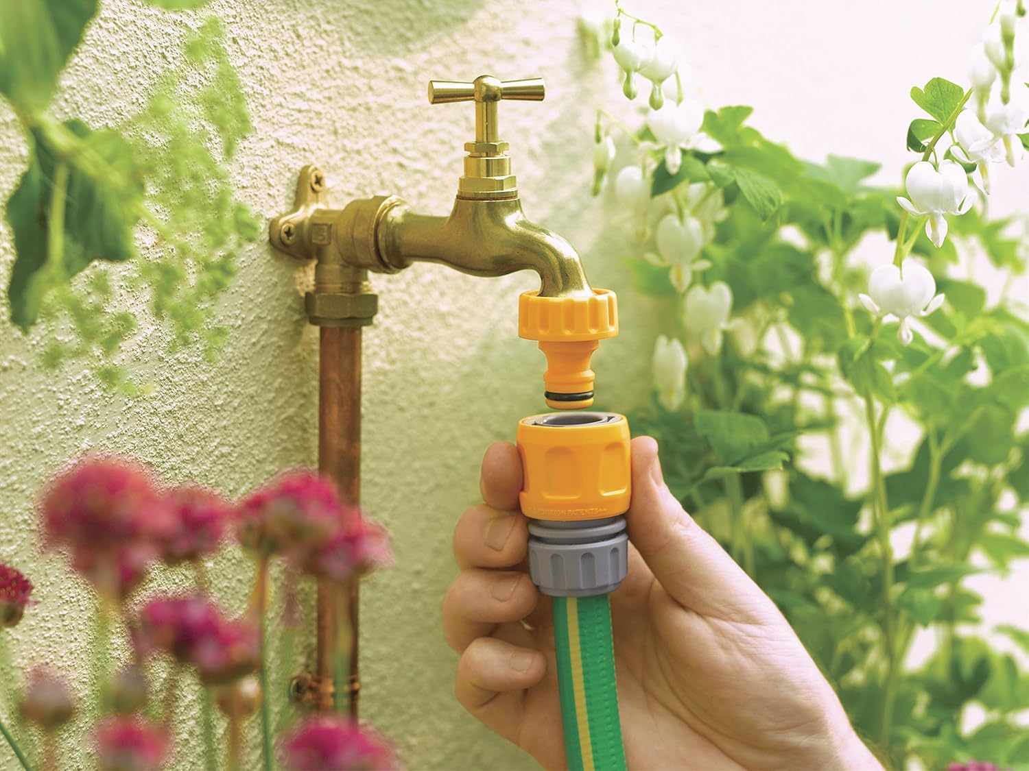 Hand connecting a garden hose fitted with a Hozelock connector to an outdoor brass garden tap