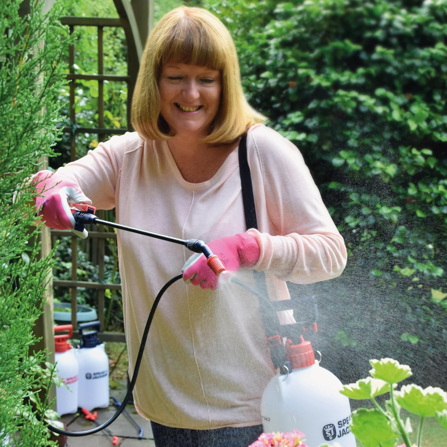 Woman wearing pink gardening gloves using the Spear & Jackson 5LPAPS sprayer to mist a flowering plant in the garden