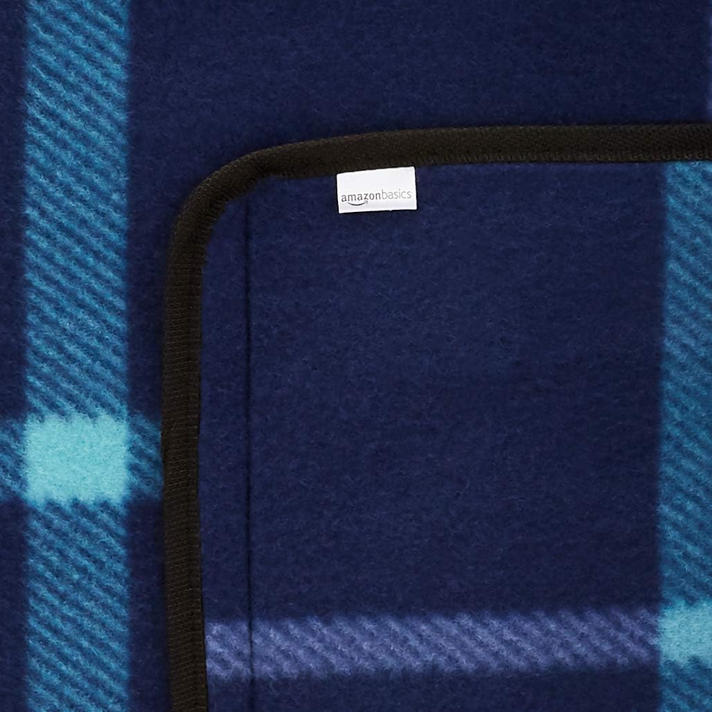 Close-up of the Amazon Basics picnic blanket corner showing the black trim edging and Amazon Basics label on the blue check fleece