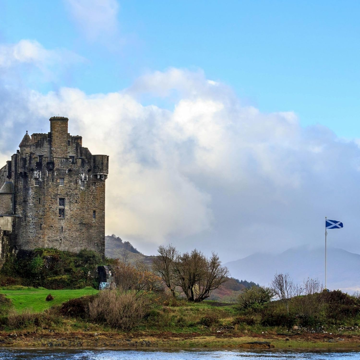 Saltire flying from a tall flagpole beside a Scottish castle and loch
