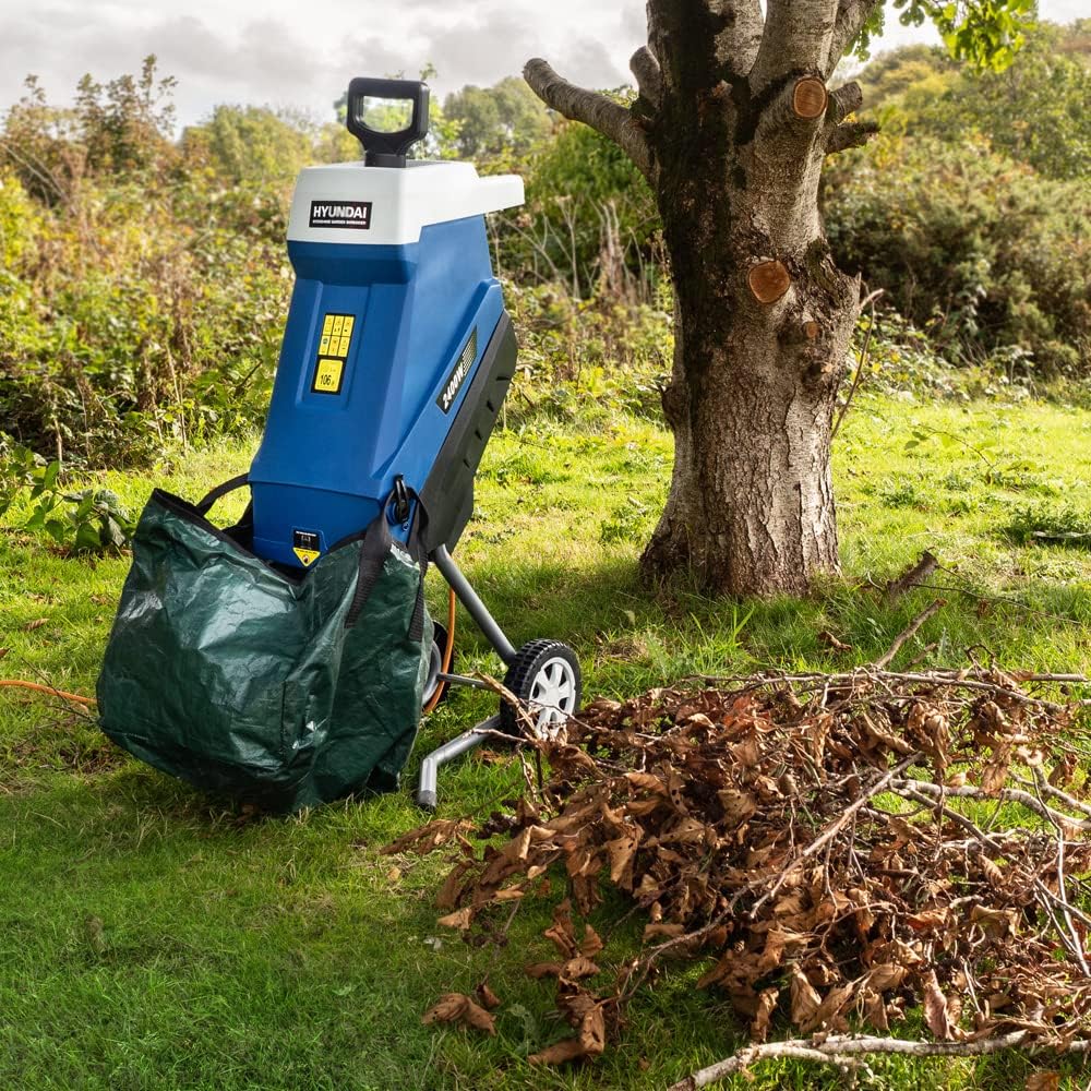 The Hyundai shredder parked on grass beside a heap of dry brown leaves and cut branches under a freshly pruned tree
