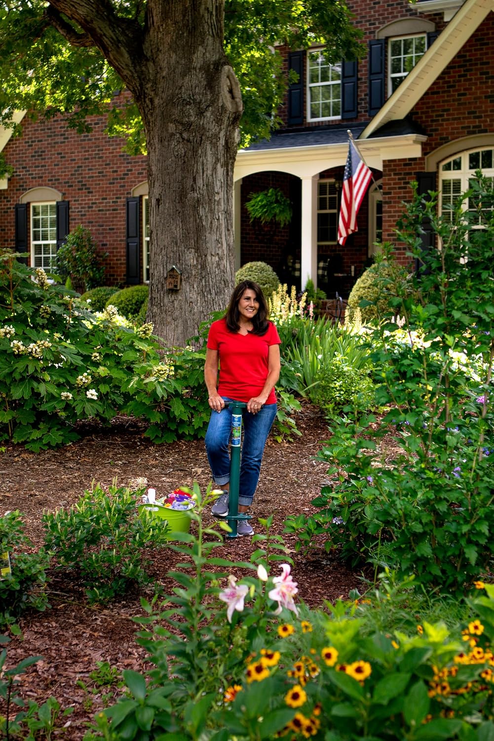 Gardener resting on the ProPlugger in a mulched border planted with lilies and rudbeckia