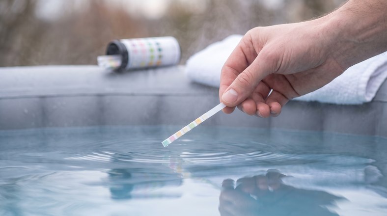 Hot tub test strip being checked above the water to catch the chemistry drift that turns hot tub water cloudy