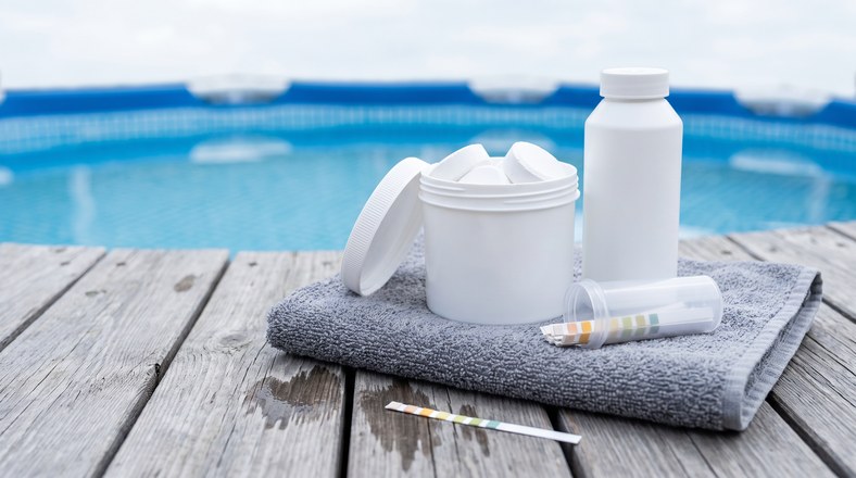 Pool test strips, chlorine tablets and winter algaecide laid out for balancing an above ground pool before winter