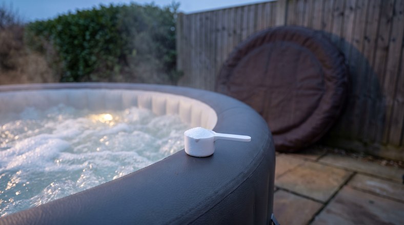 Scoop of shock dose granules beside churning hot tub jets with the cover off in a UK garden
